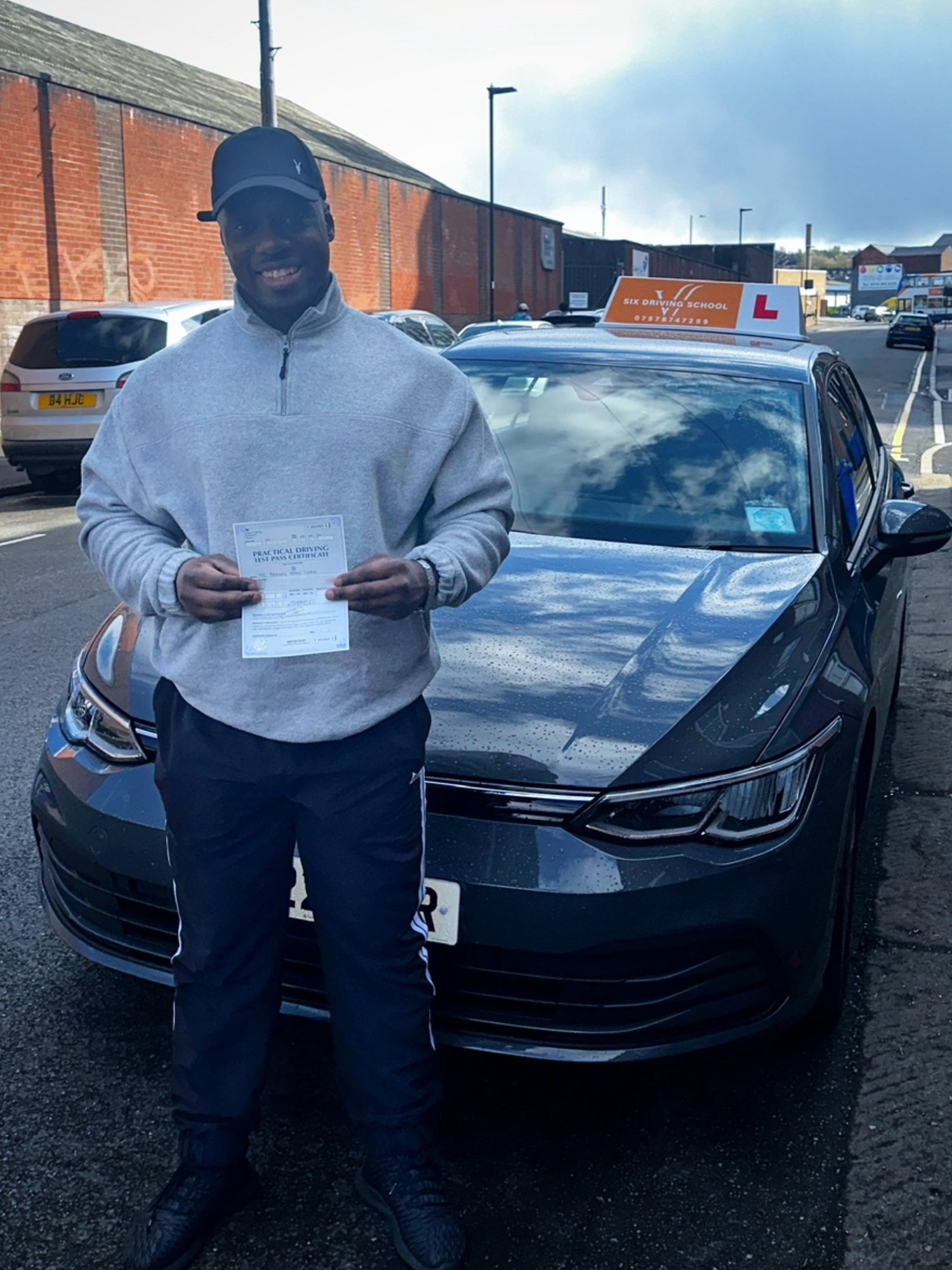 Max with a pass certificate beside the Six Driving School car